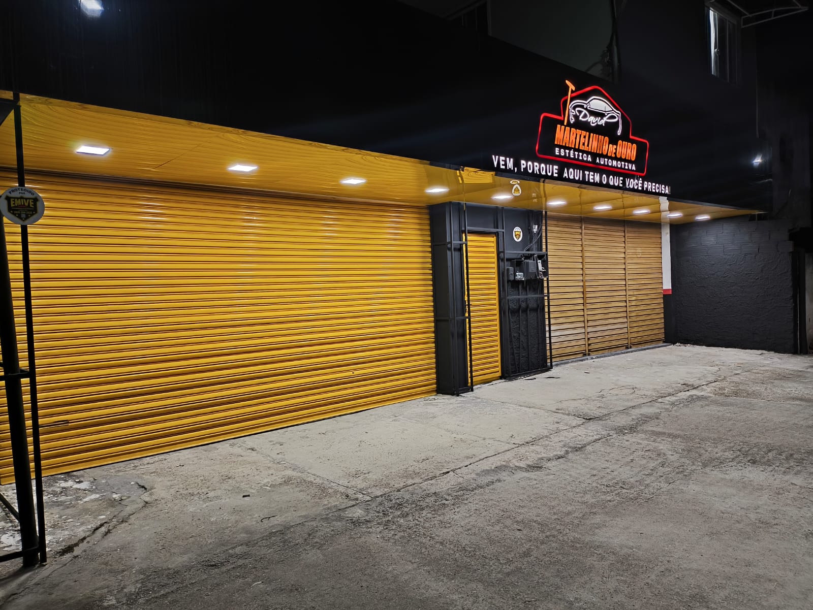 Fachada iluminada à noite, com logo em neon e portas amarelas